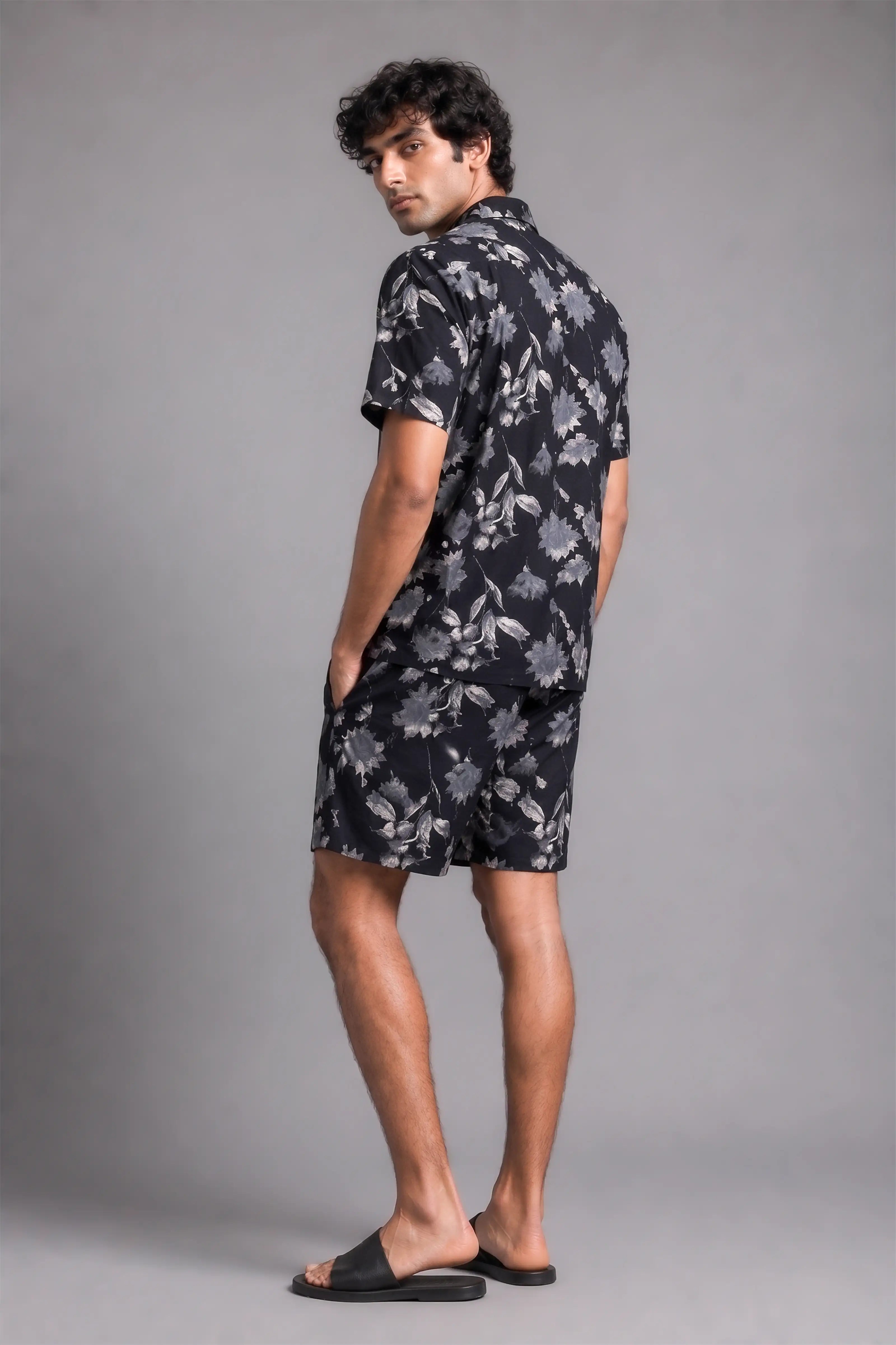 Man wearing a black floral shirt and shorts on a gray background