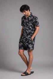 Man wearing a black floral shirt and shorts on a gray background