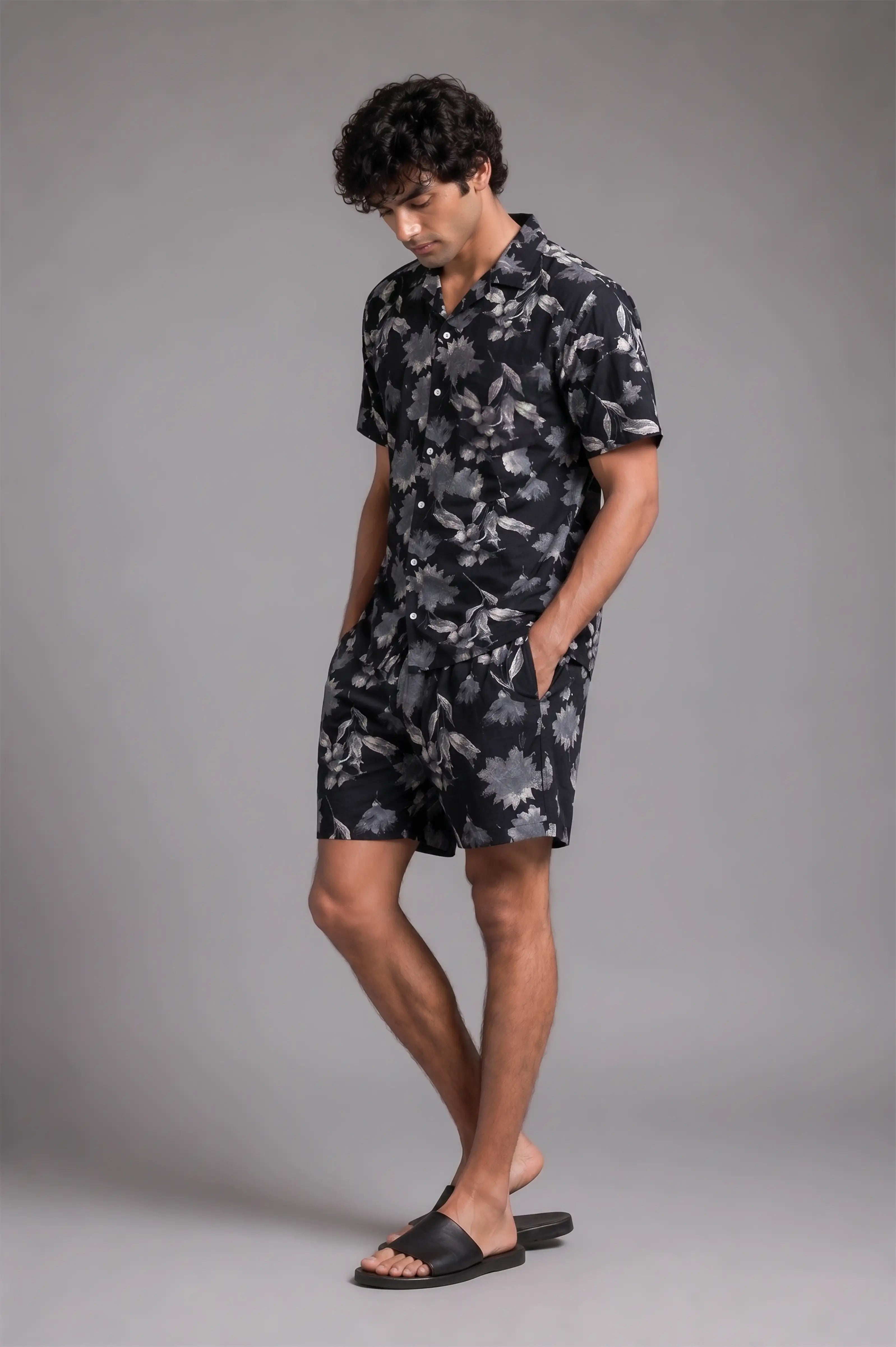 Man wearing a black floral shirt and shorts on a gray background