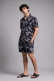 Man wearing a black floral shirt and shorts on a gray background