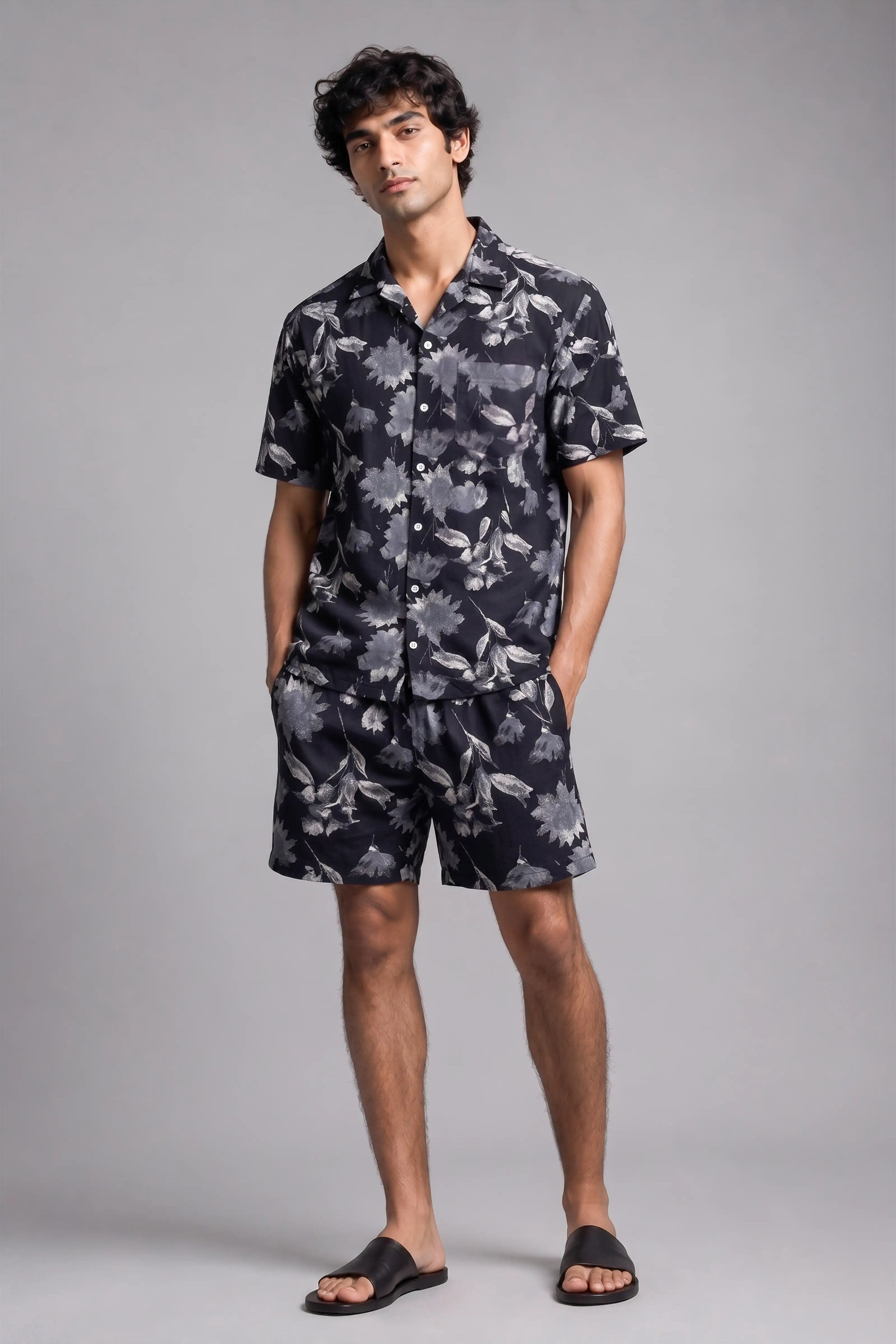 Man wearing a dark floral shirt and shorts on a gray background