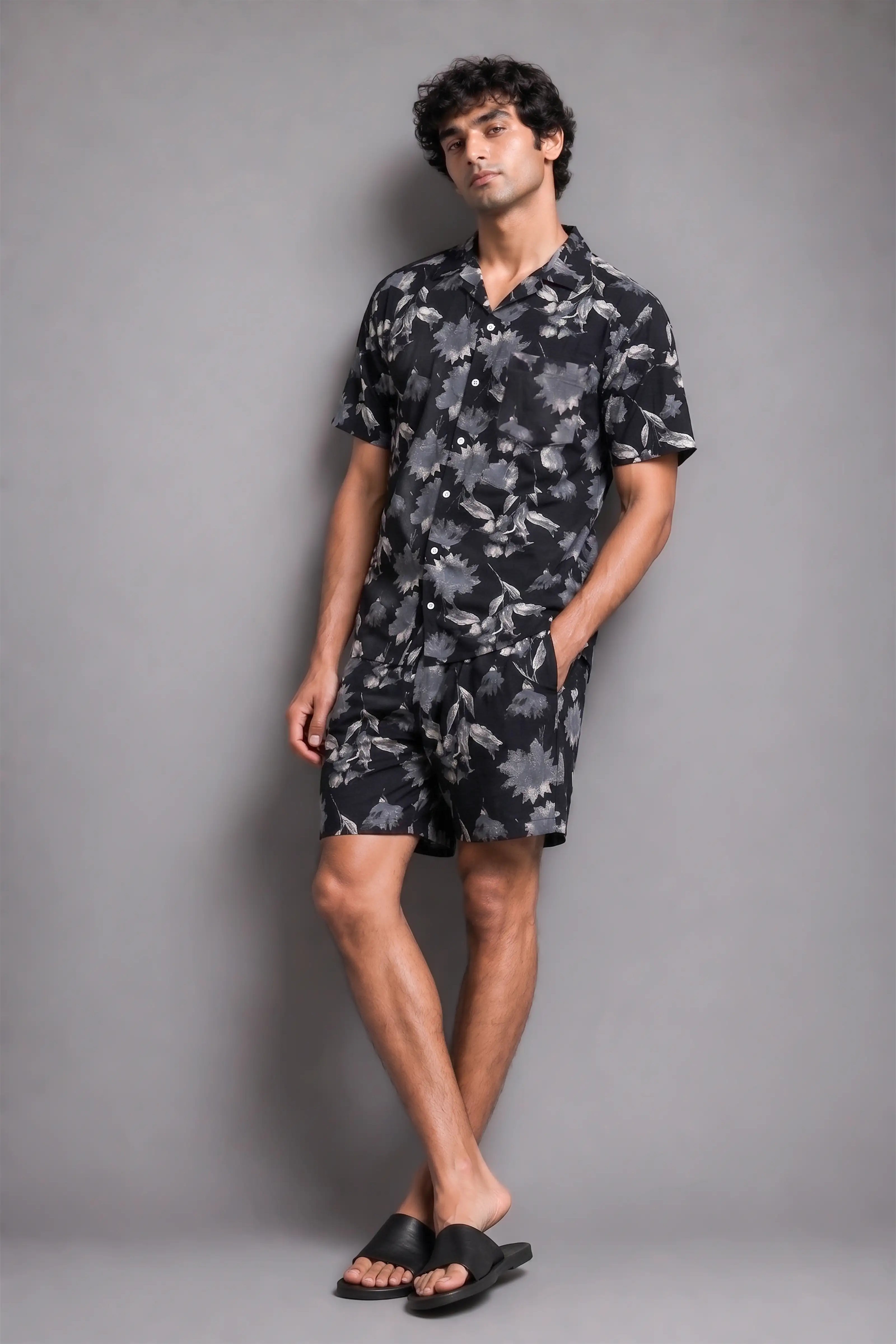 Man wearing a black floral shirt and shorts against a gray background