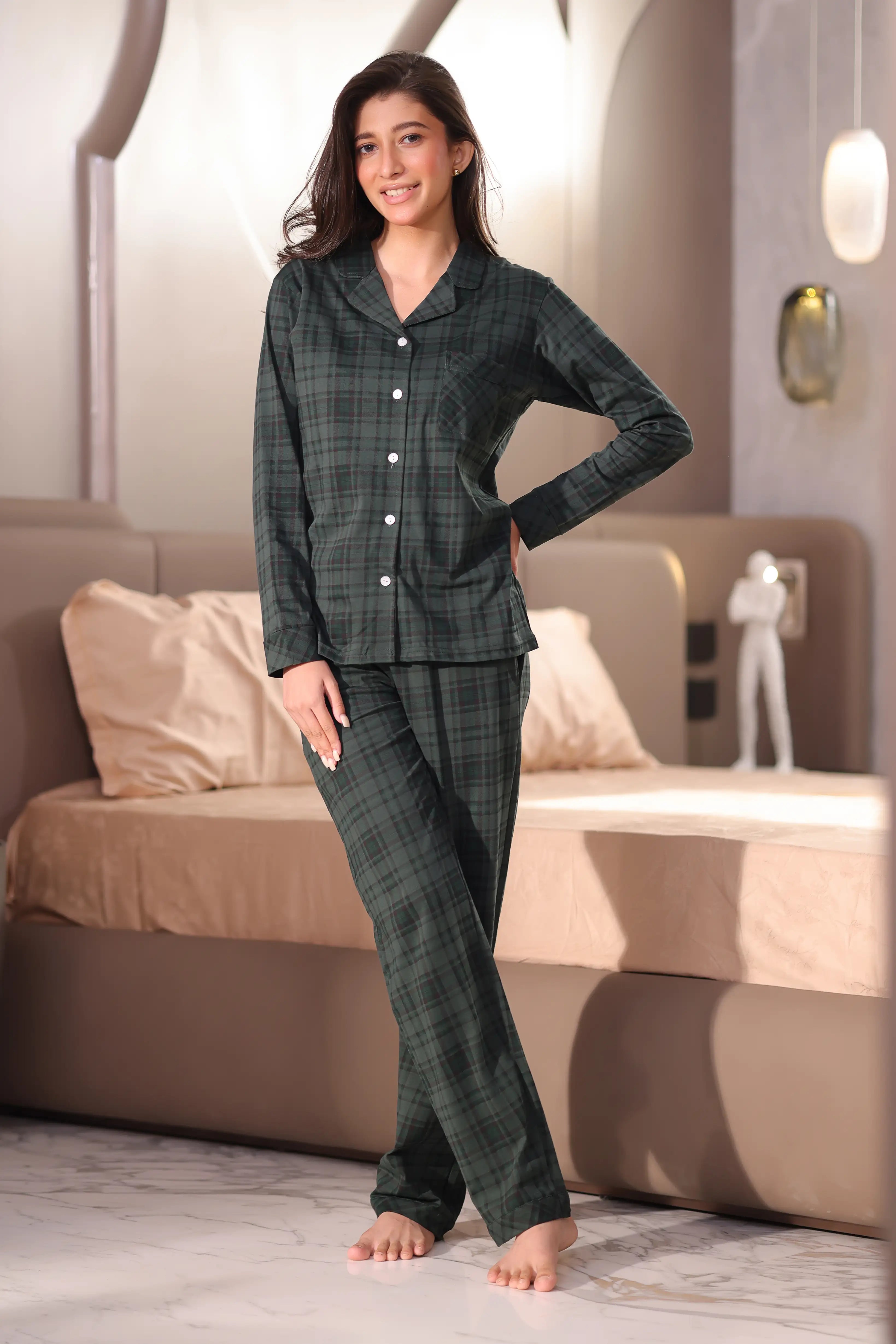 A woman wearing a green plaid pajama set in a bedroom.