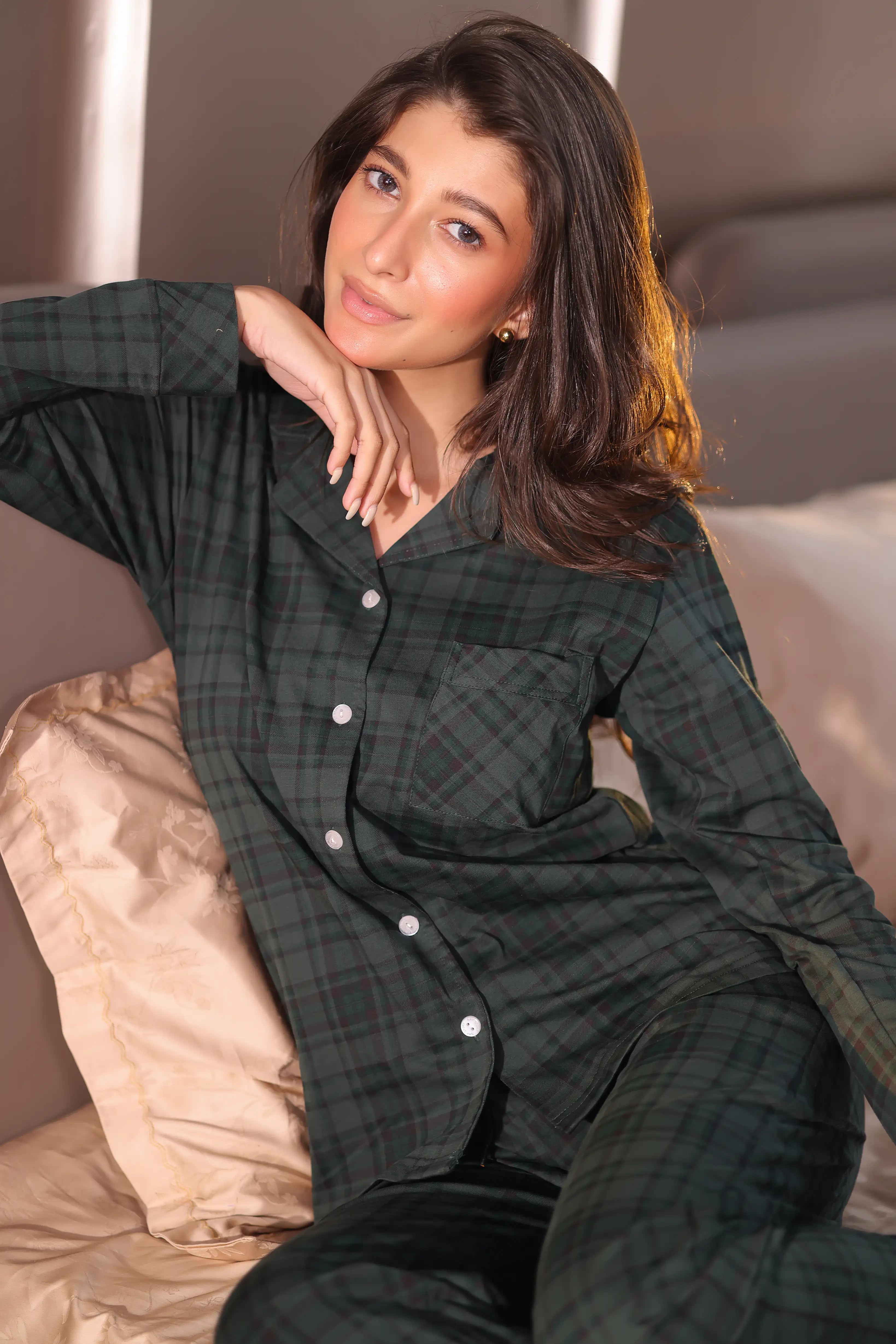 Woman wearing a green plaid pajama set sitting on a couch.