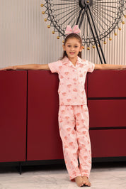 Girl in a pink pajama set standing against a red cabinet with decorative elements in the background.
