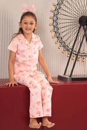 A girl in a pink pajama set with jellyfish print pattern, sitting on a red surface, ferris wheel in the background.