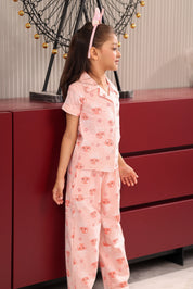 A girl in a pink jellyfish print pajama set, standing next to a red dresser.