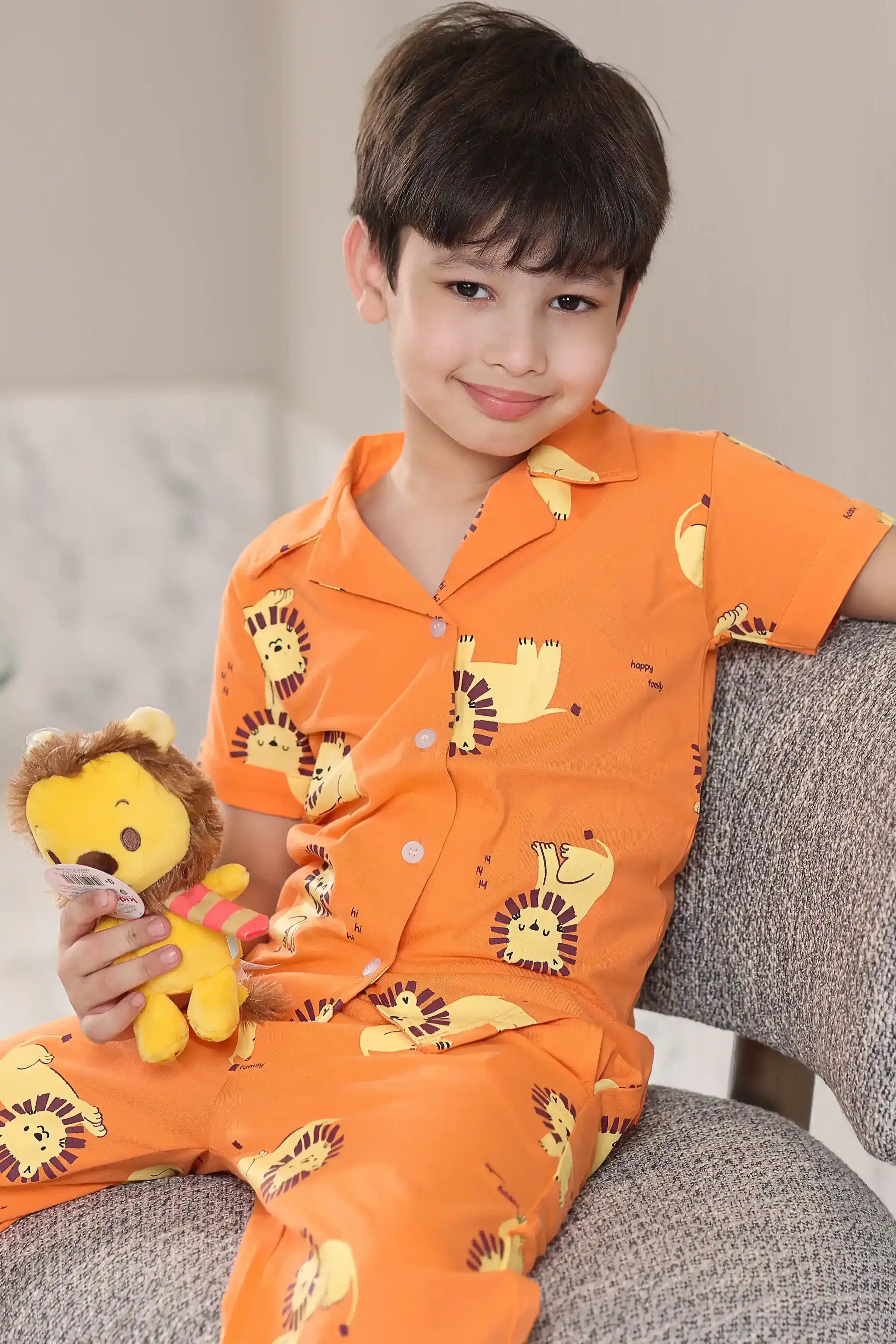 Child wearing orange pajamas with lion-print animal patterns, holding a plush toy, sitting on a couch.