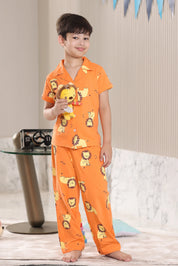 Child wearing orange pajamas with lion print, holding a plush toy, in a room setting.