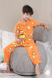 A child in an orange pajama set with lion print sitting on a gray ottoman.