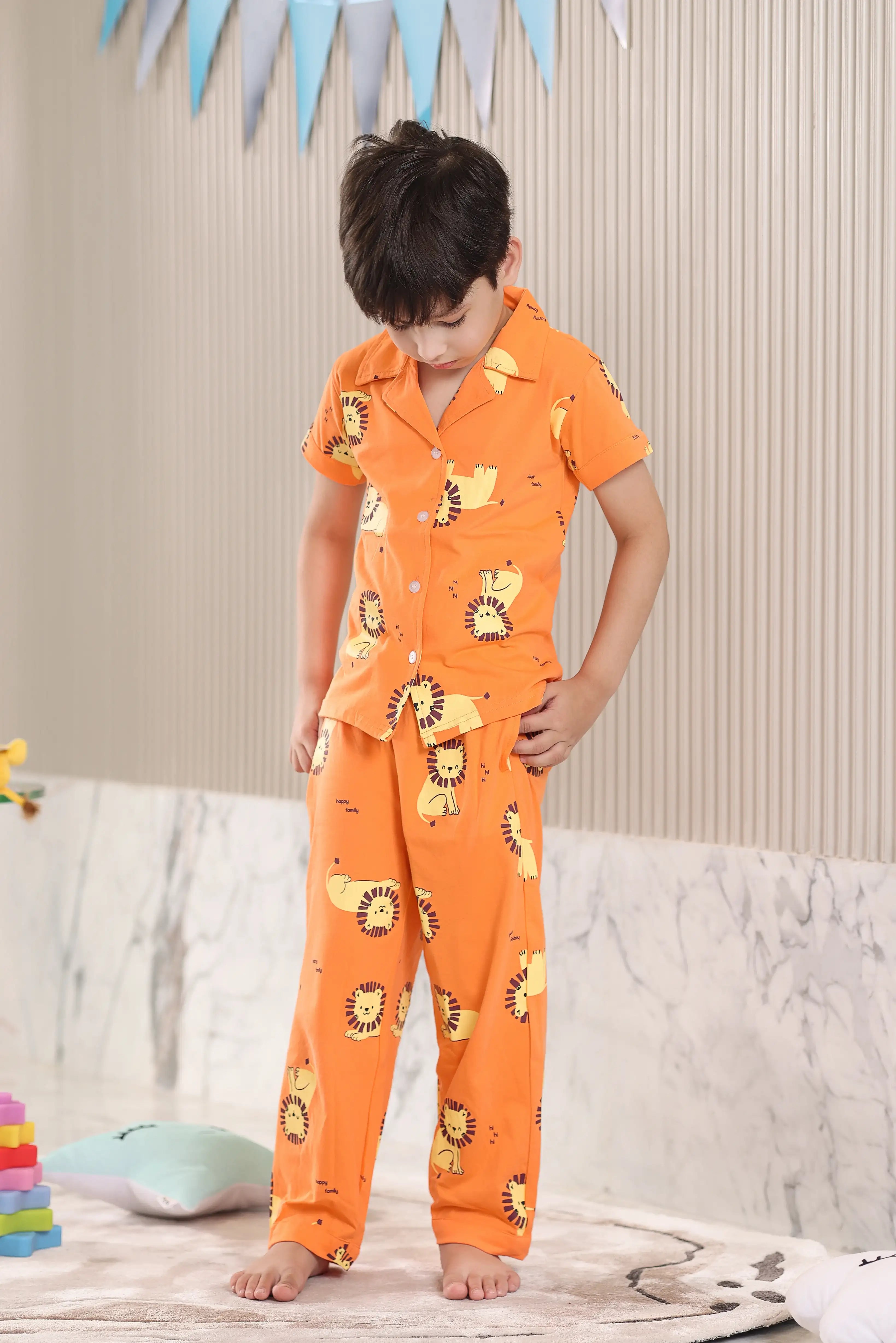 A child wearing orange pajamas with lion prints in a room setting.