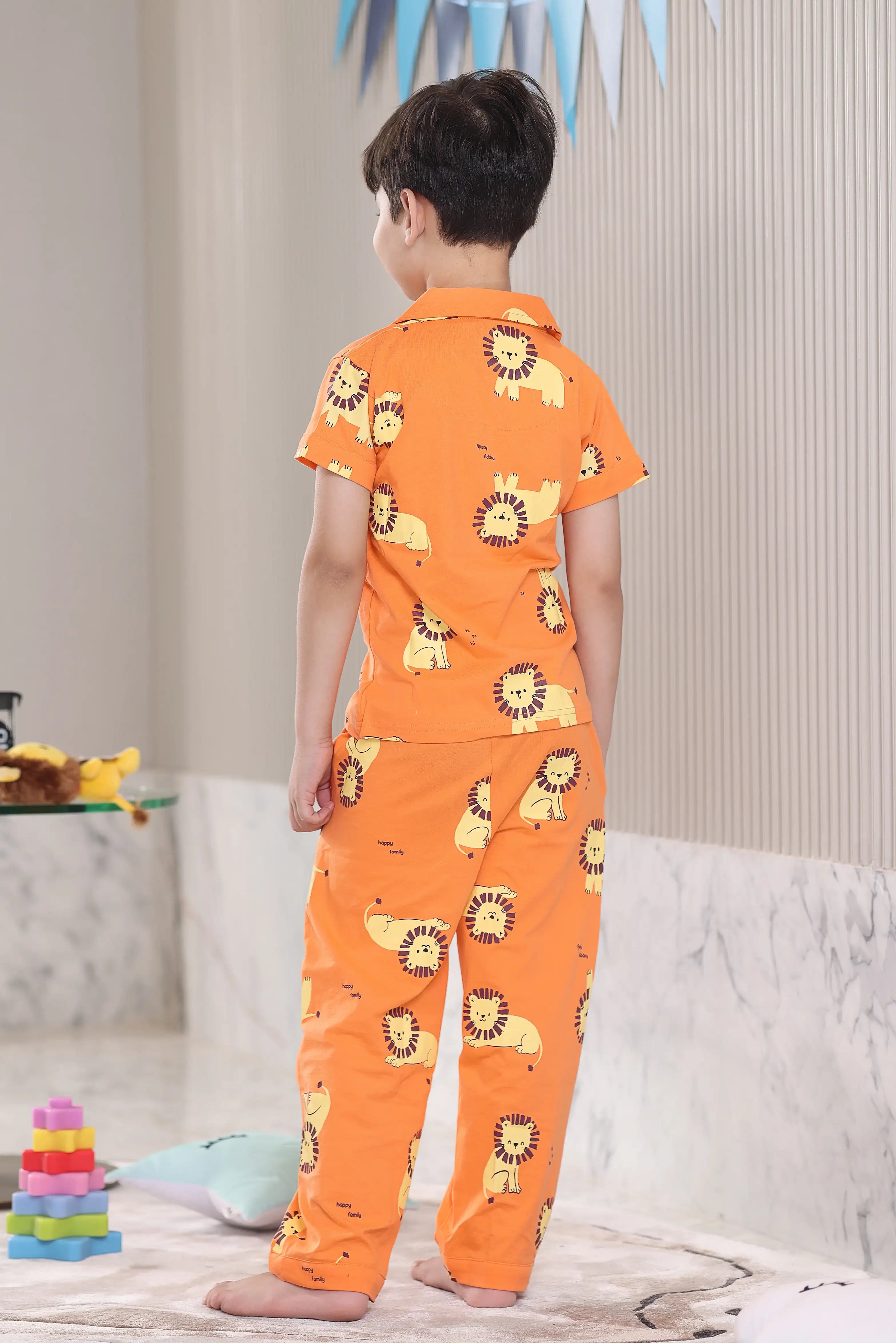 A child wearing an orange pajama set with lion prints in a living room.