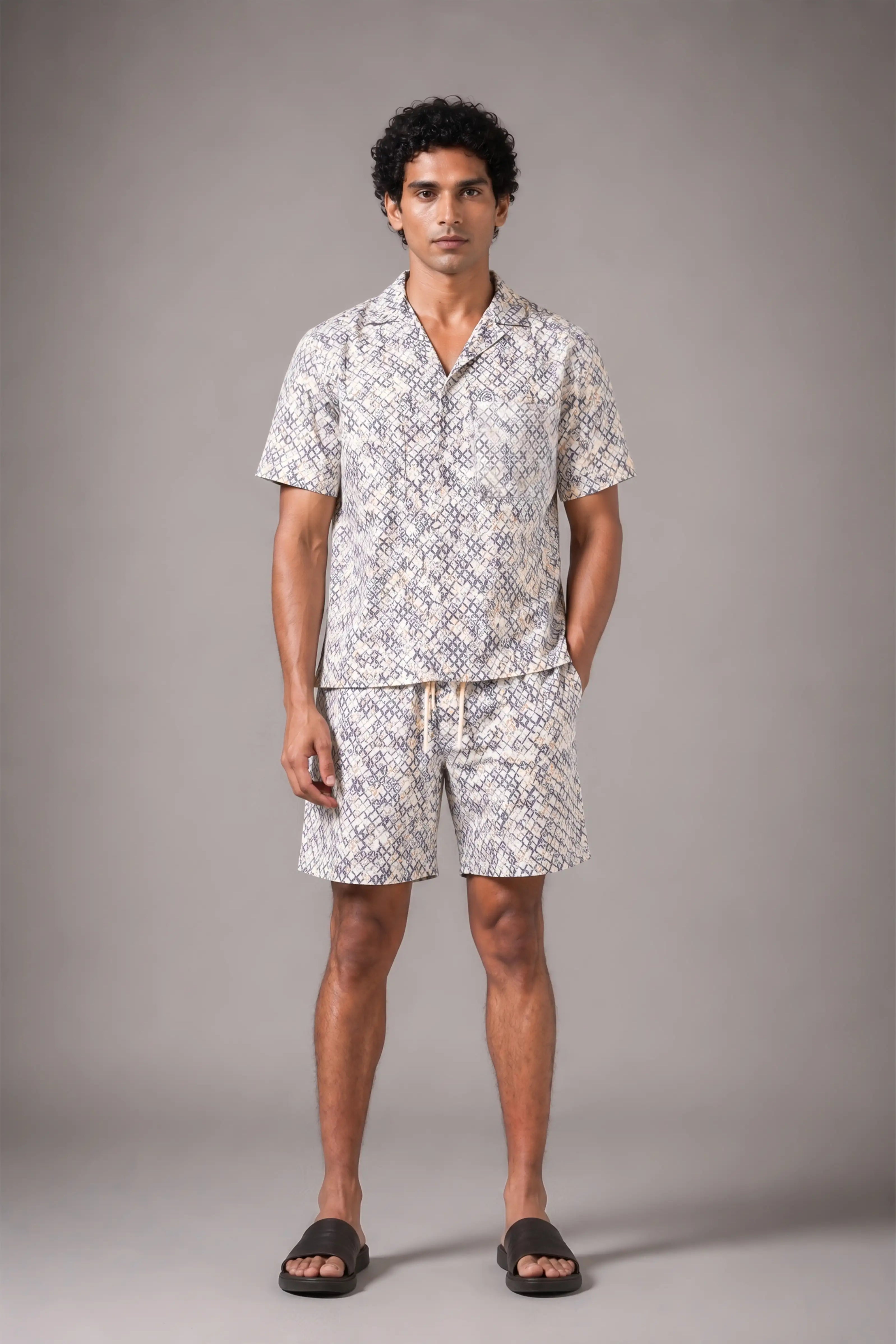 Man wearing a patterned shirt and shorts set against a gray background