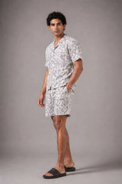 Man wearing a patterned shirt and shorts set against a gray background