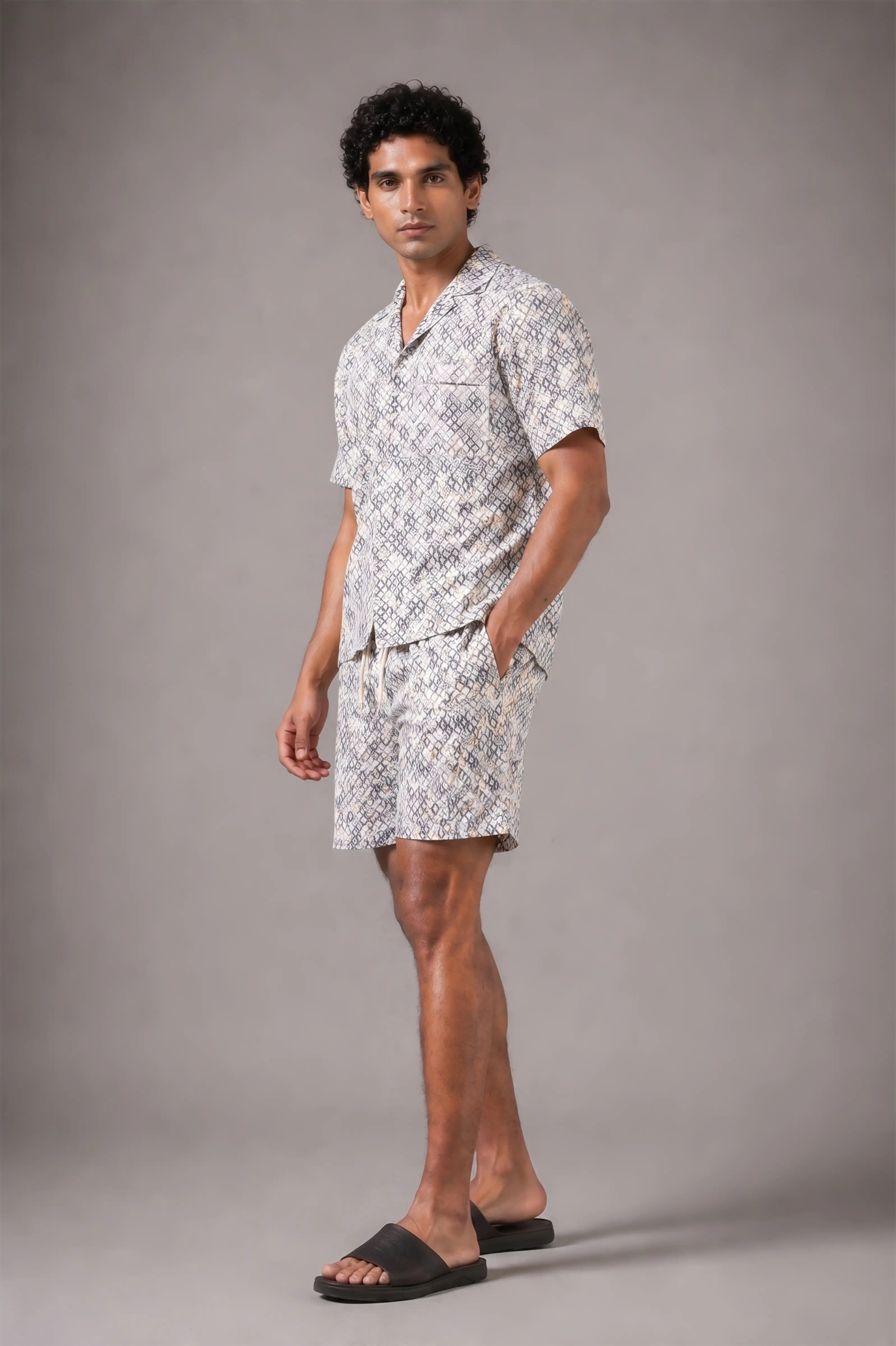 Man wearing a patterned shirt and shorts set against a gray background