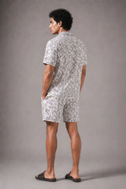 Man wearing a patterned shirt and shorts standing against a plain background