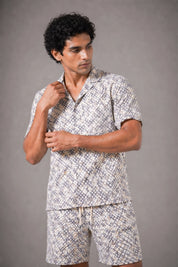 Man wearing a patterned shirt and shorts set against a gray background