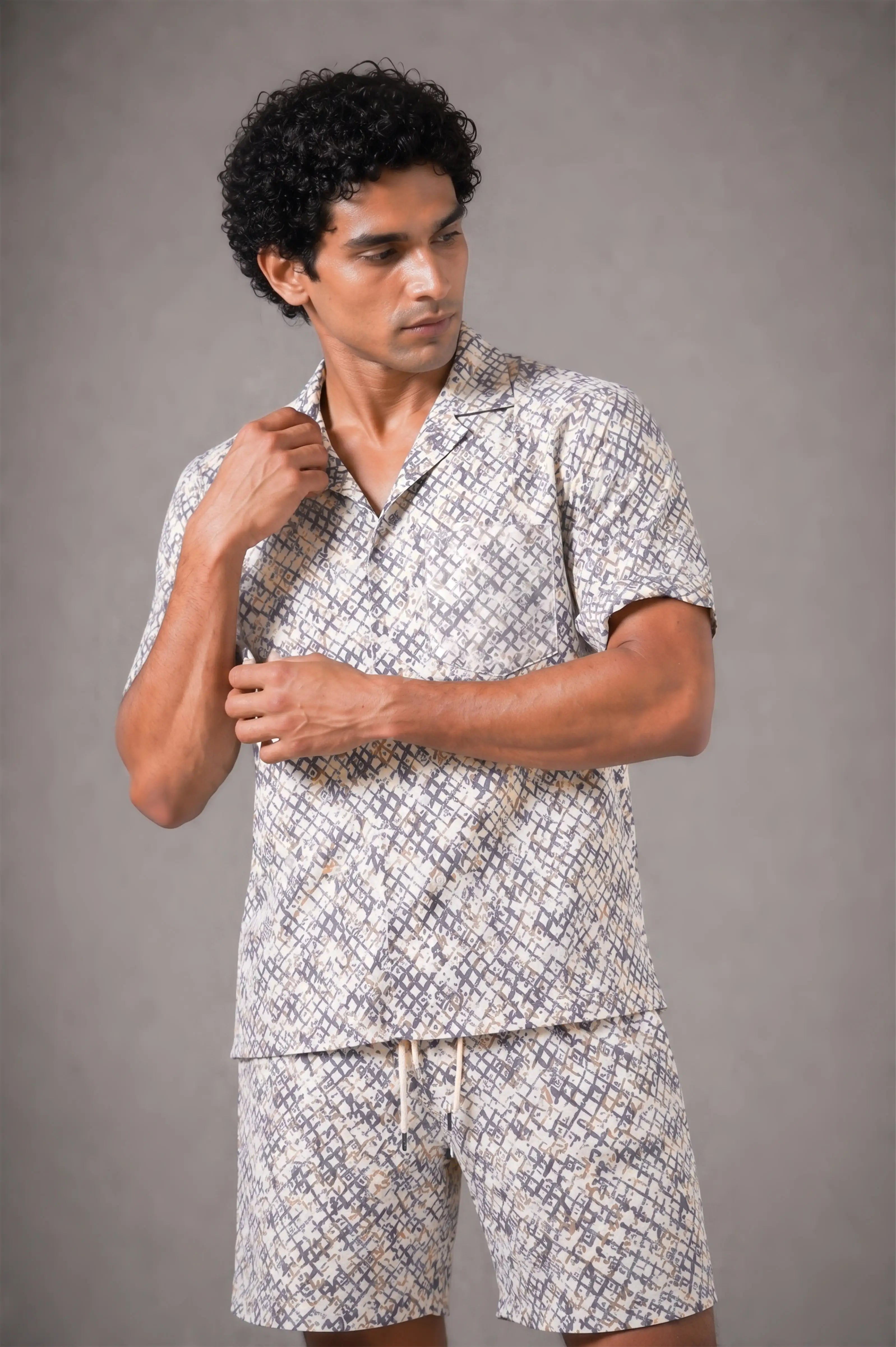 Man wearing a patterned shirt and shorts set against a gray background