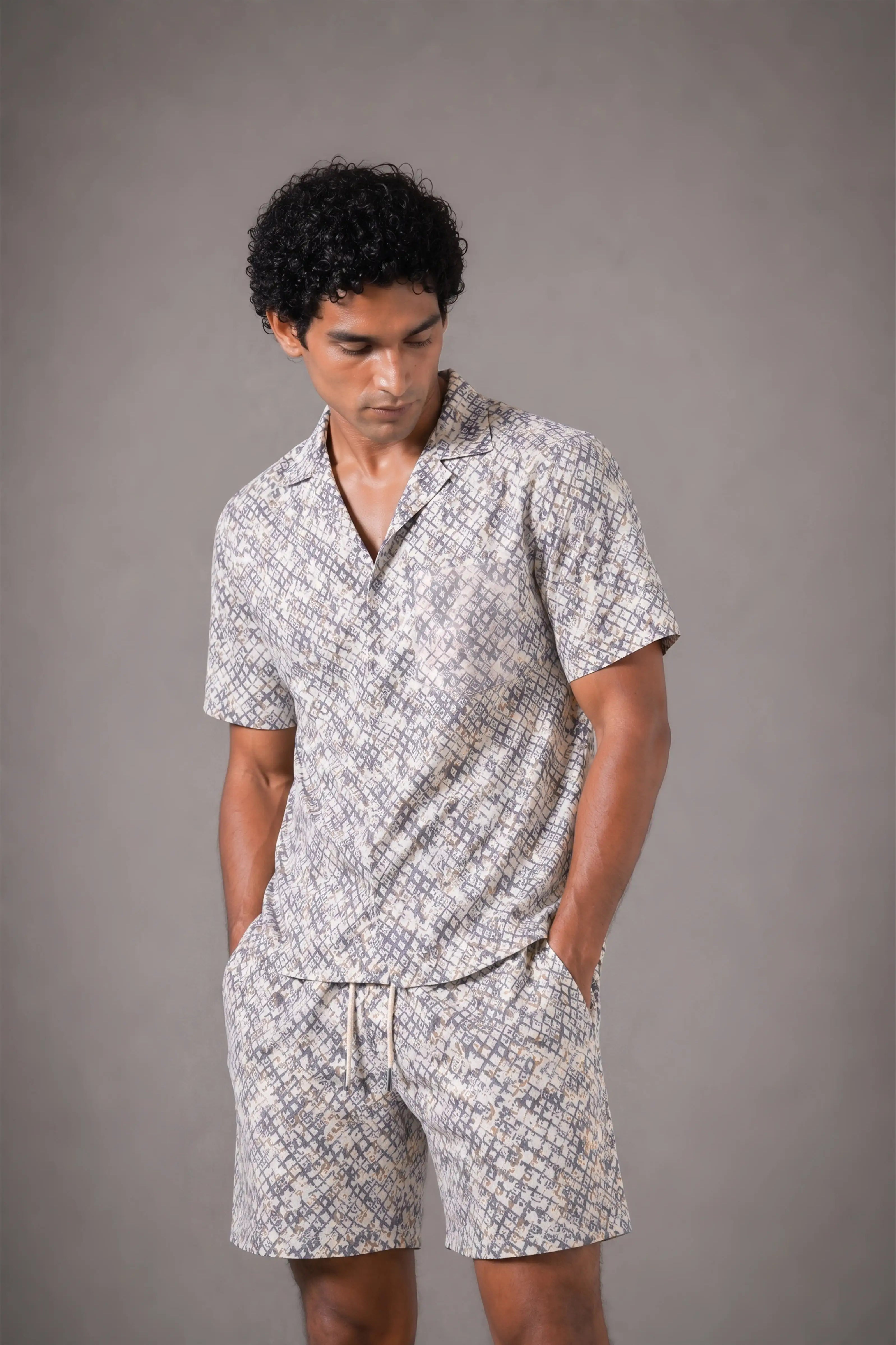 Man wearing a patterned shirt and shorts set against a gray background