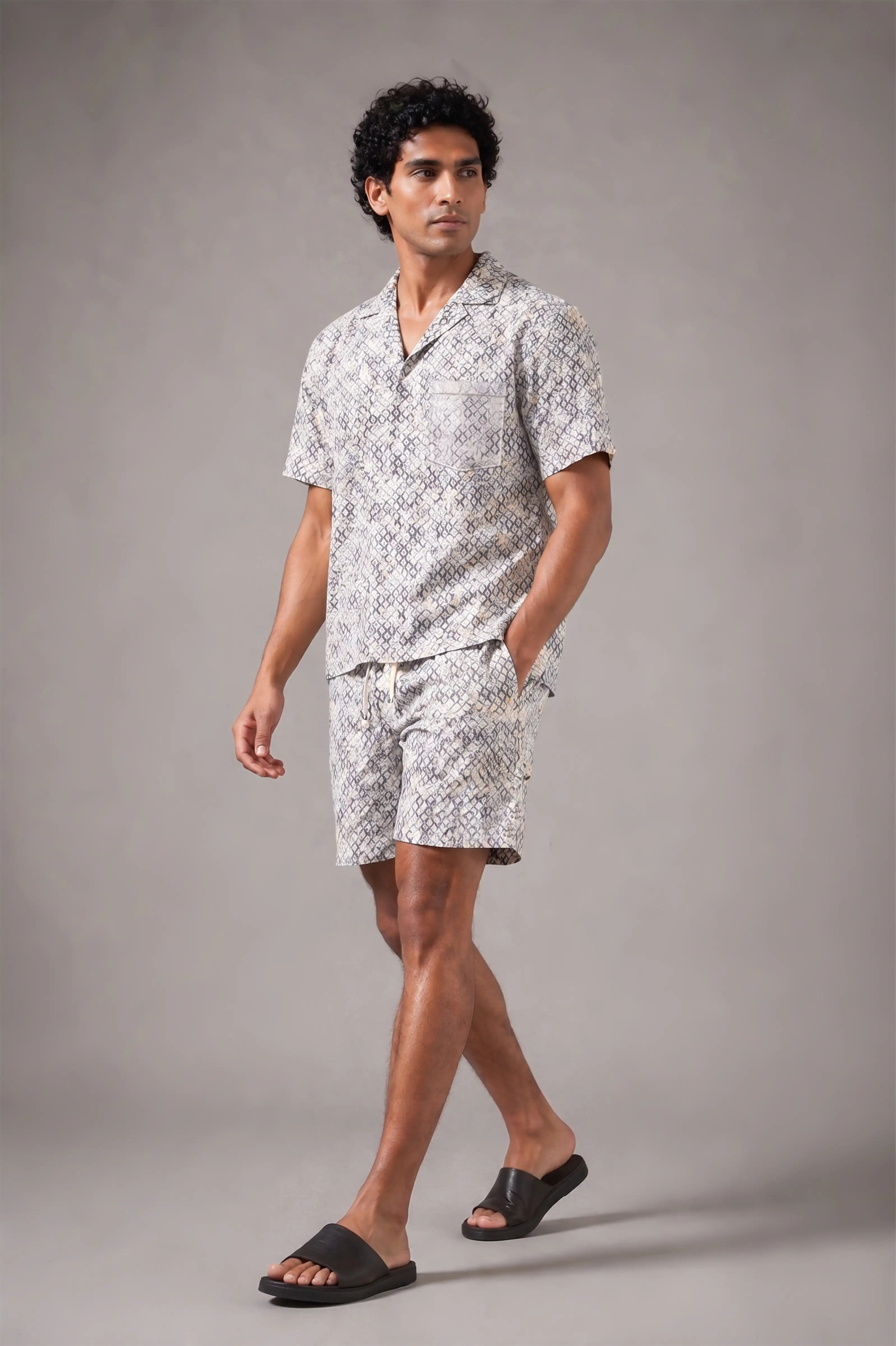 Man wearing a patterned shirt and shorts set on a gray background