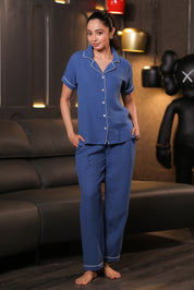 Woman wearing blue pajamas standing in a room with a couch and decorative items.