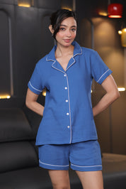 Woman wearing a blue shorts set with white piping in a room setting.