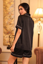 Woman wearing a black shorts set in a cozy room with a lamp and decorative items.