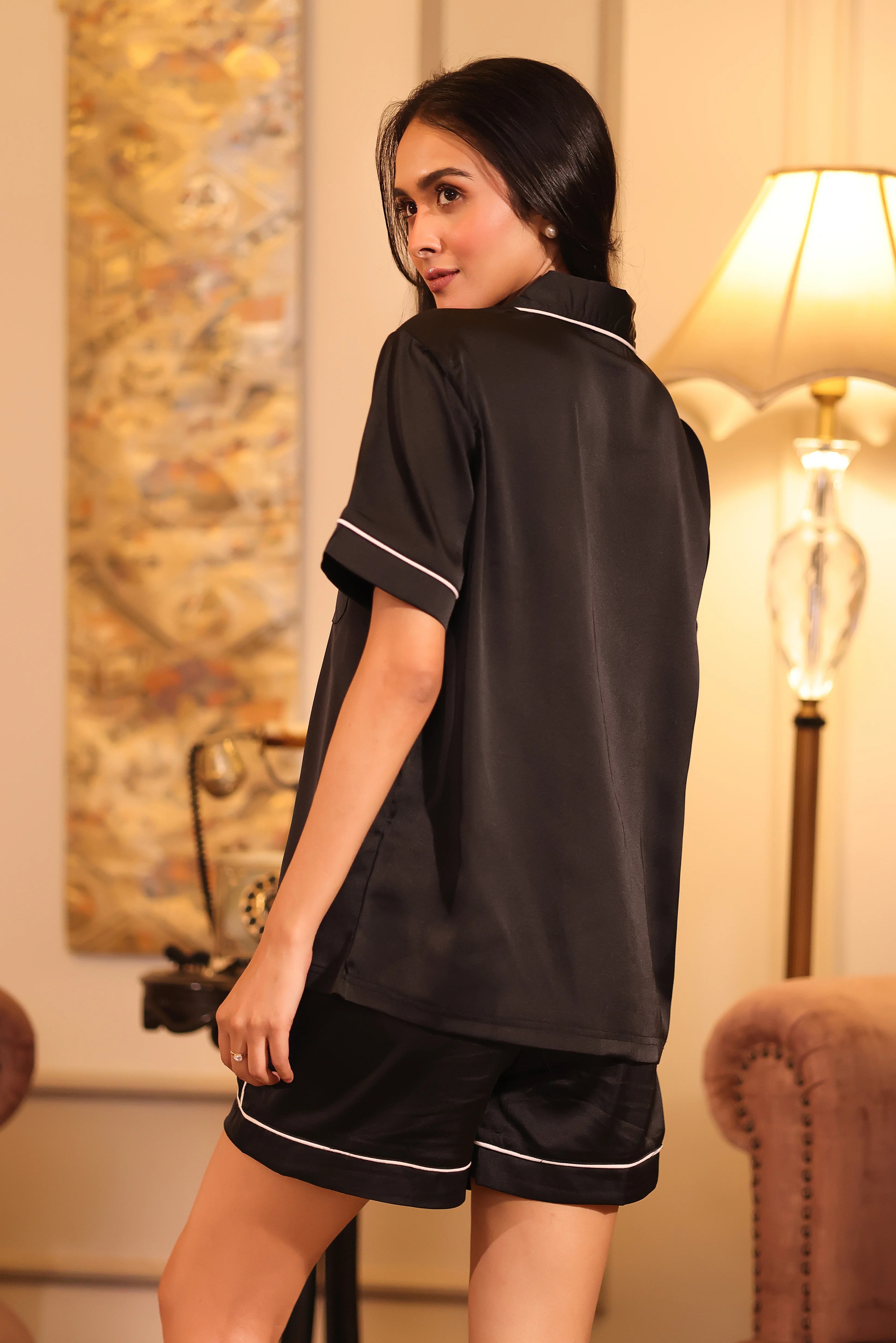 Woman wearing a black shorts set in a cozy room with a lamp and decorative items.
