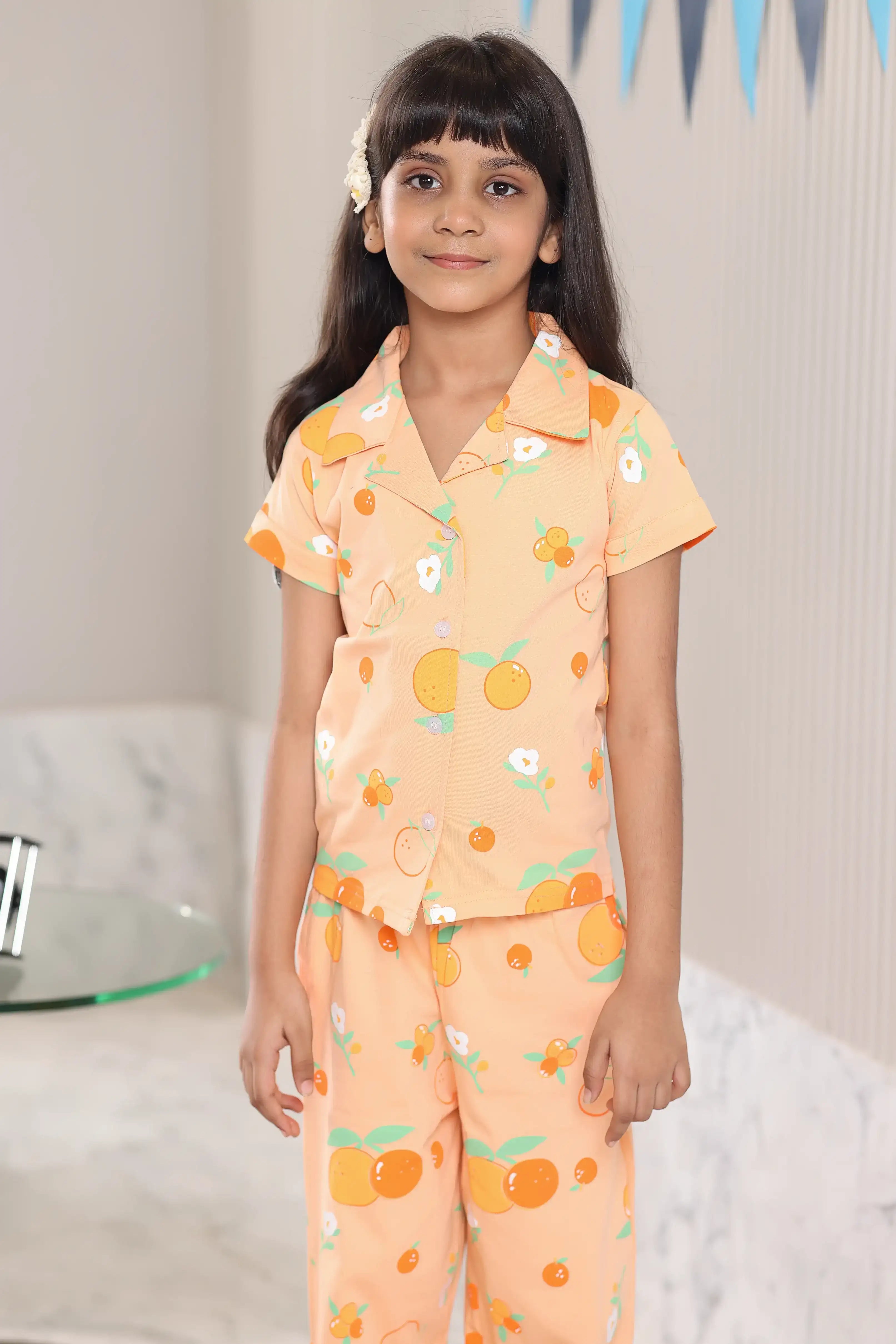 A girl wearing an orange-colored pajama set with an orange fruit pattern indoors.