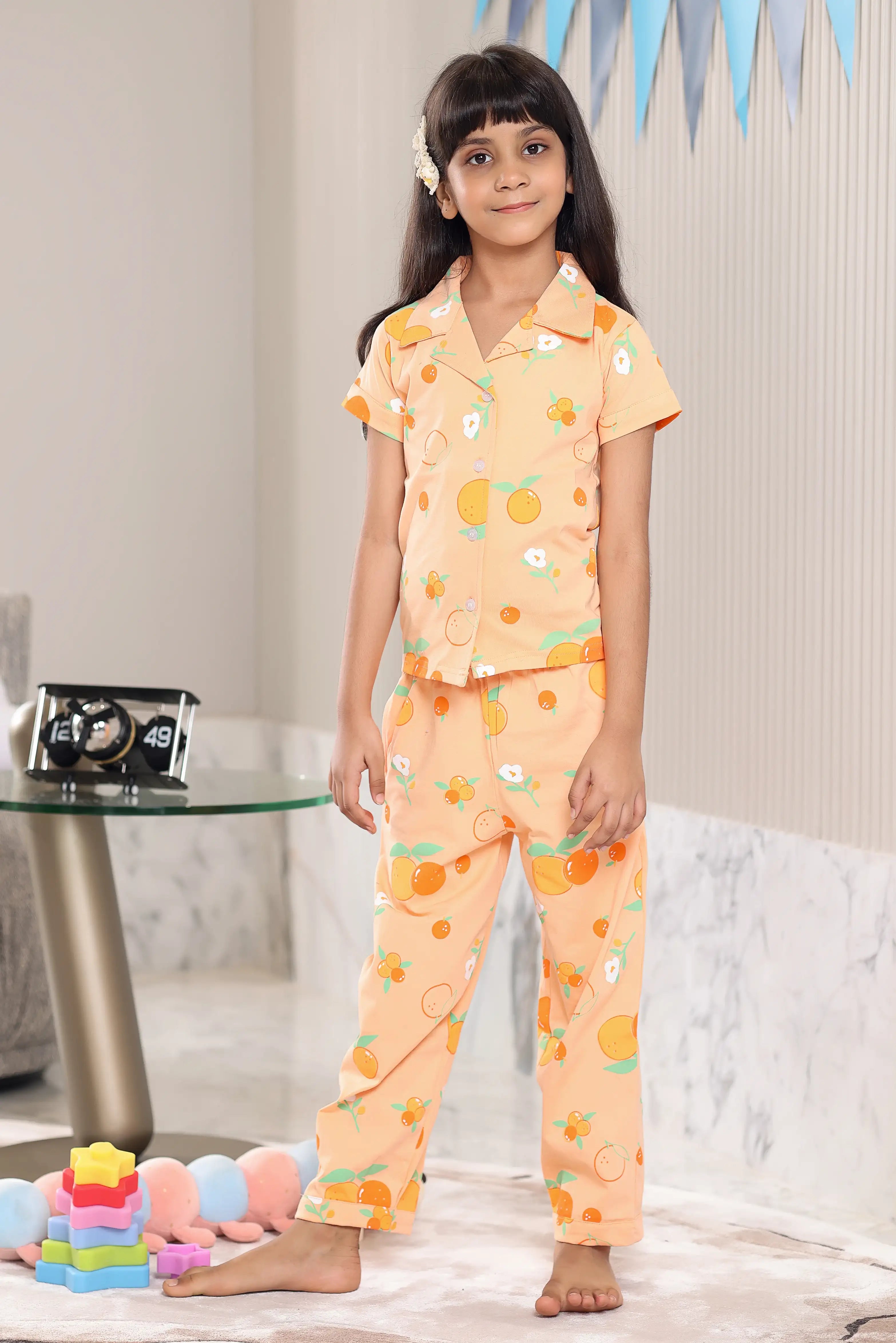 A girl wearing a matching Orange pajama set with an orange fruit pattern in a room.