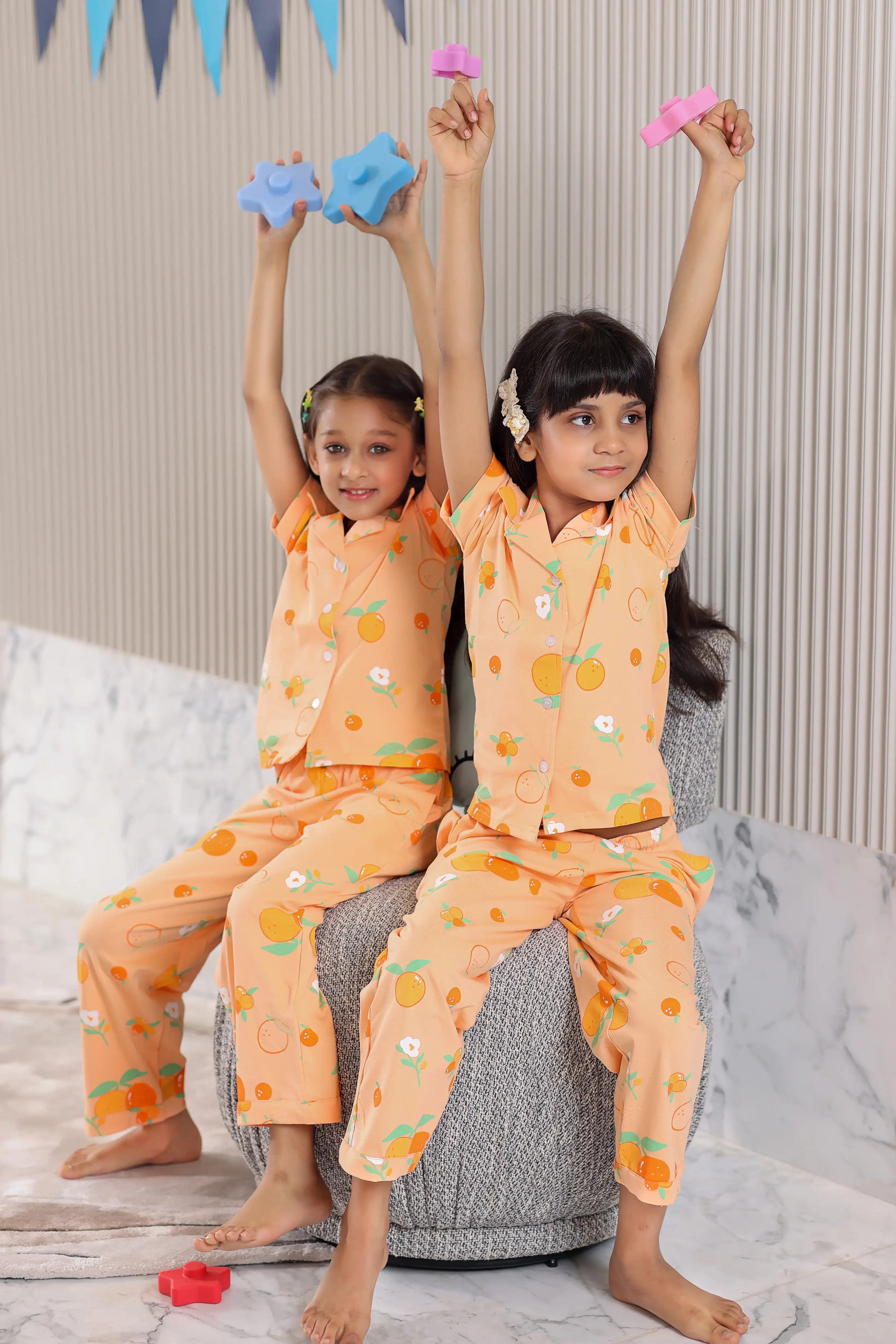 Two children in matching orange pajamas sitting on a bean bag chair.