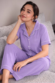 Woman wearing a purple pajama set sitting on a couch.