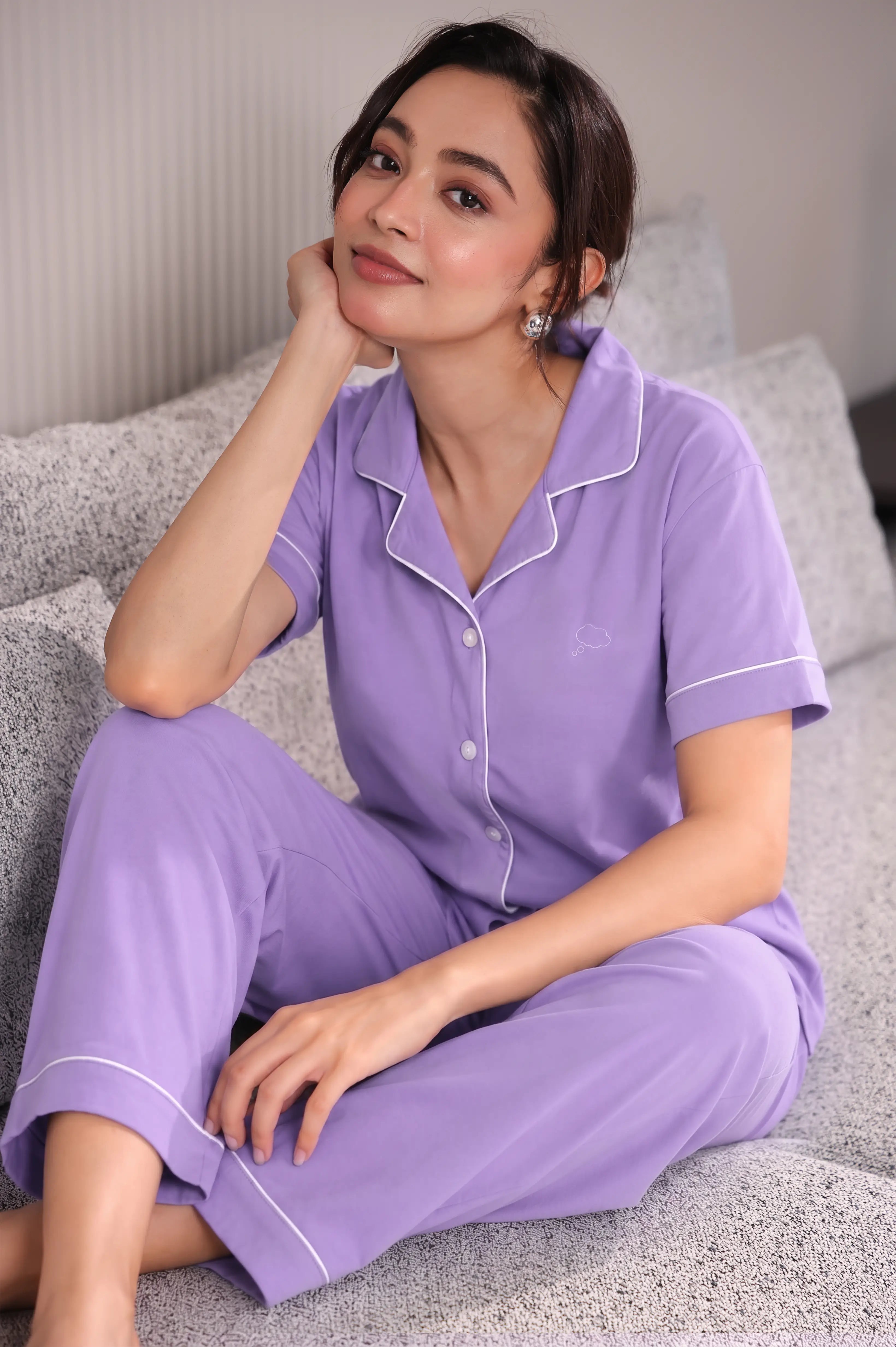 Woman wearing a purple pajama set sitting on a couch.