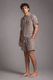 Man wearing a checkered shirt and shorts set against a gray background