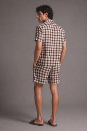 Man wearing a checkered shirt and shorts set against a gray background