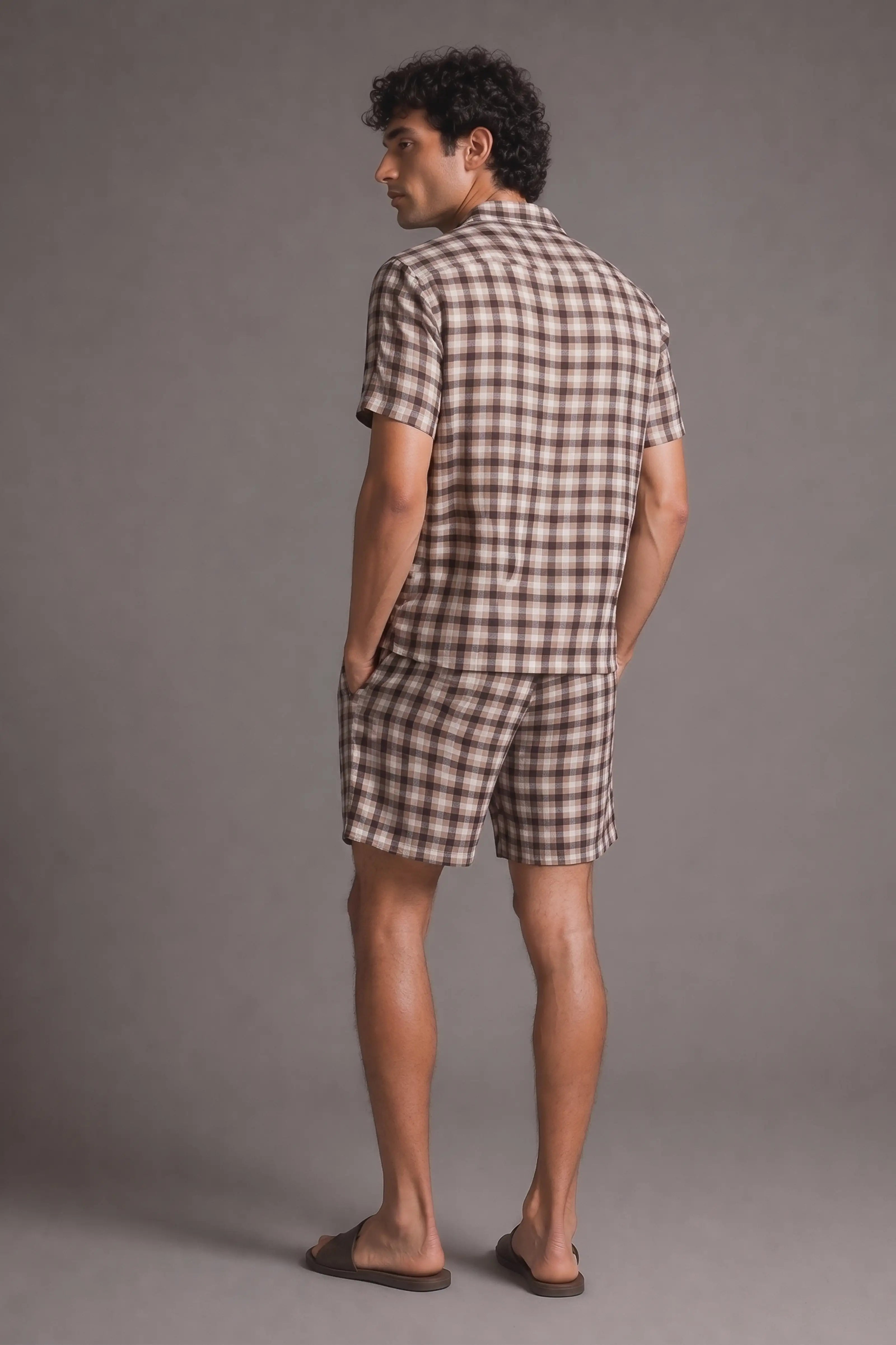 Man wearing a checkered shirt and shorts set against a gray background