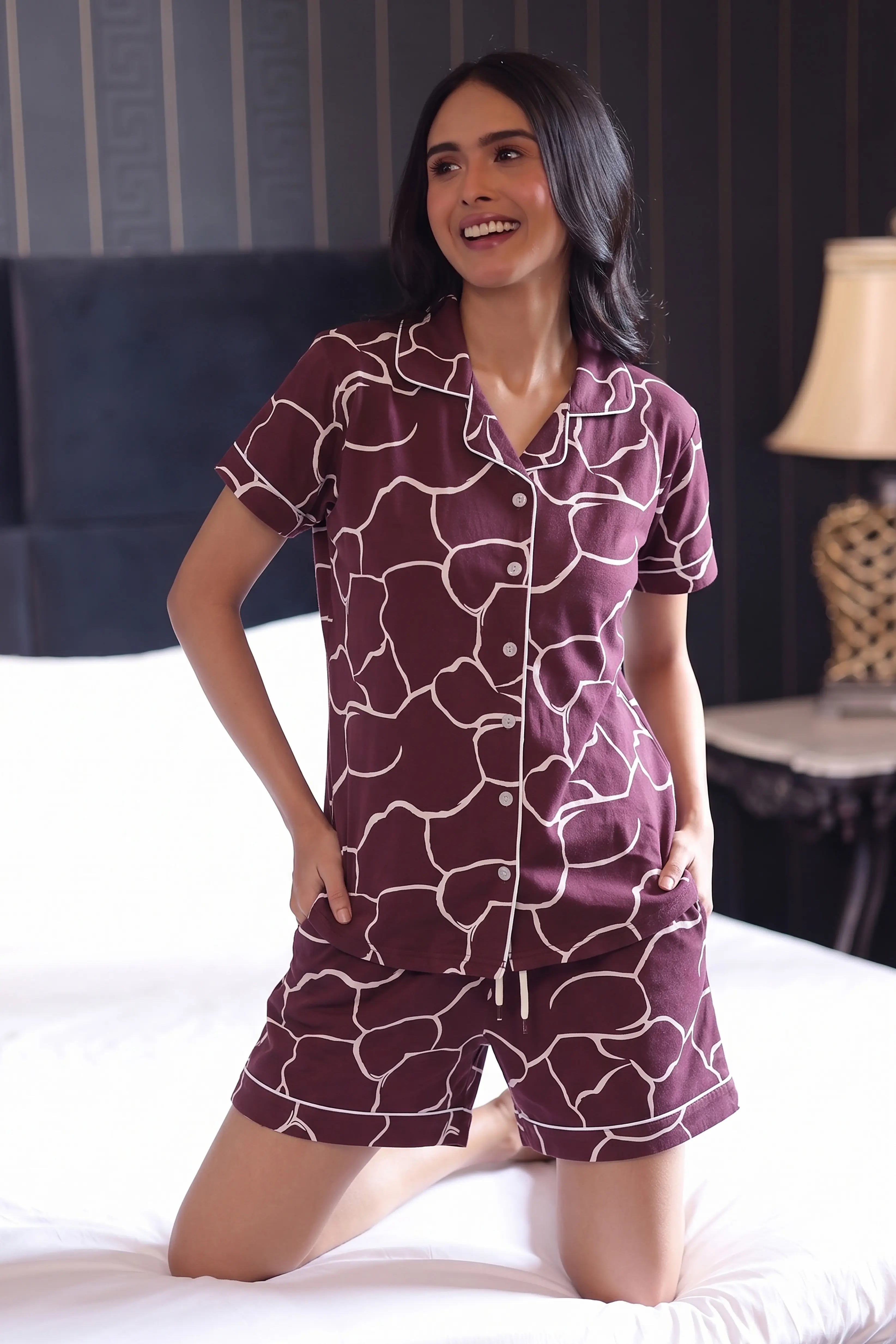 Woman wearing a patterned shorts set sitting on a bed in a bedroom.