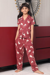 A child wearing a maroon pony print pyjama set with white patterns in a room.