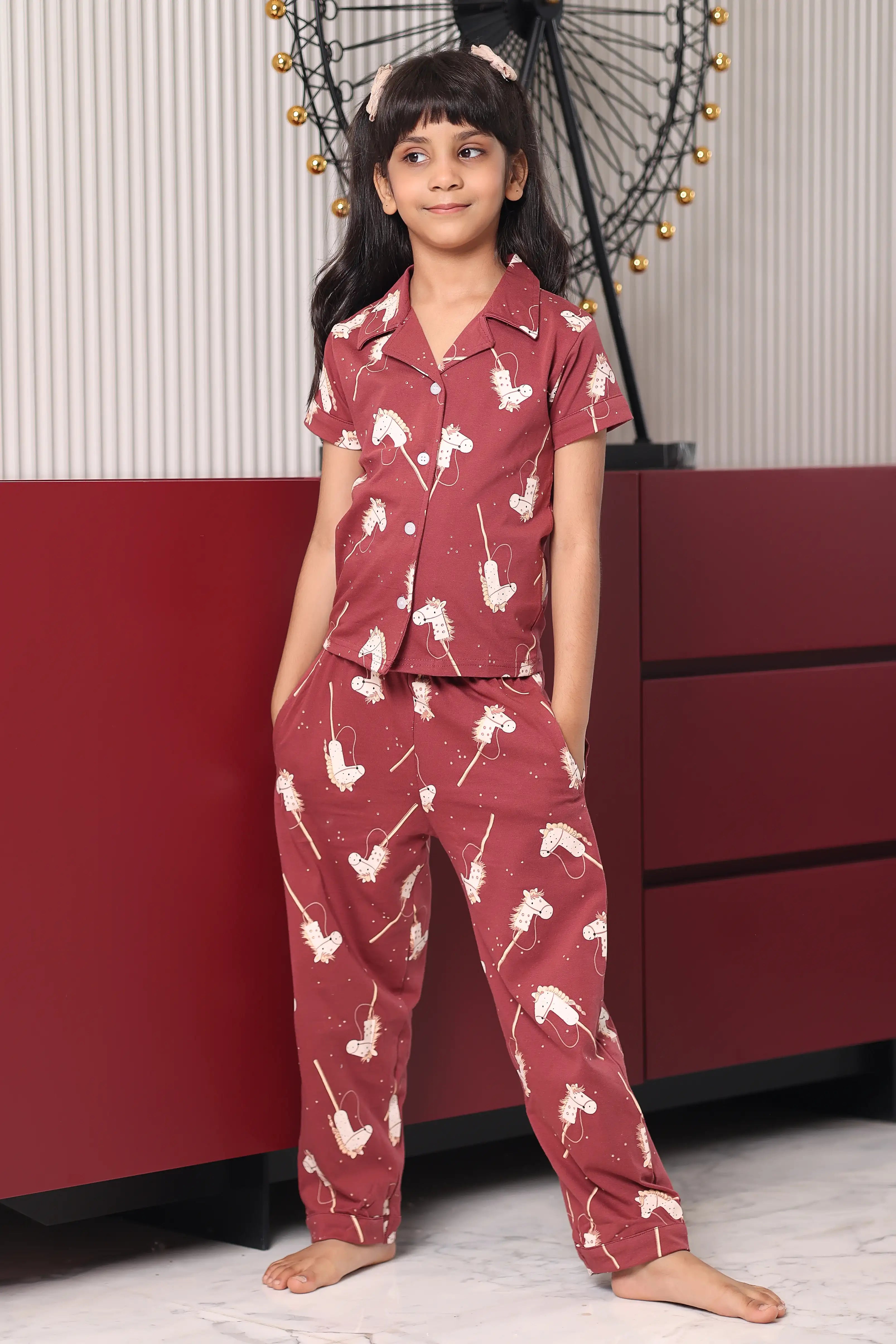 A child wearing a maroon pony print pyjama set with white patterns in a room.