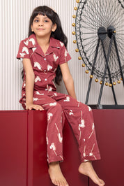 A child wearing a maroon print pajama set with pony patterns, sitting on a red surface.
