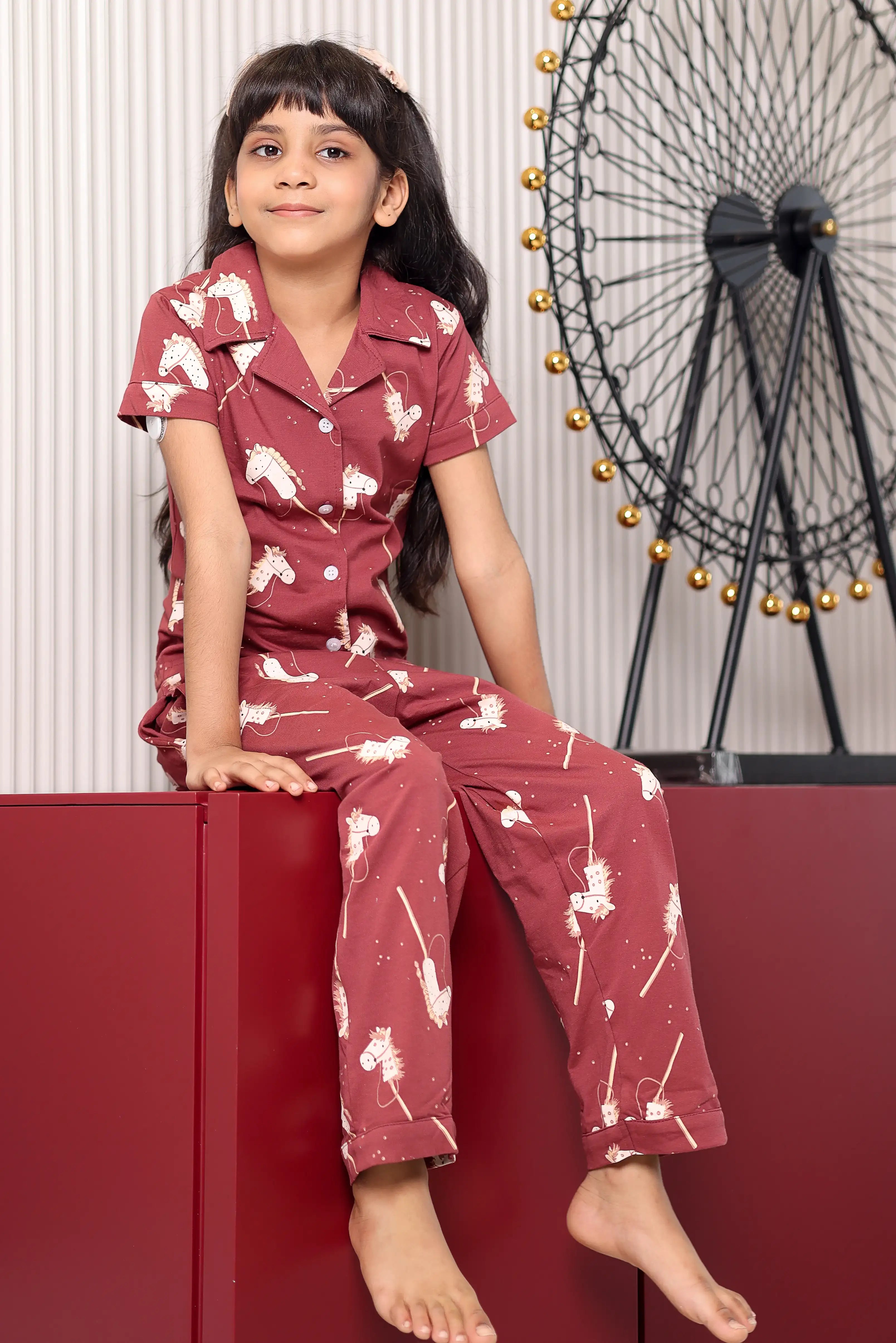 A child wearing a maroon print pajama set with pony patterns, sitting on a red surface.