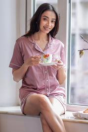 Woman in pink shorts set holding a floral teacup by a window