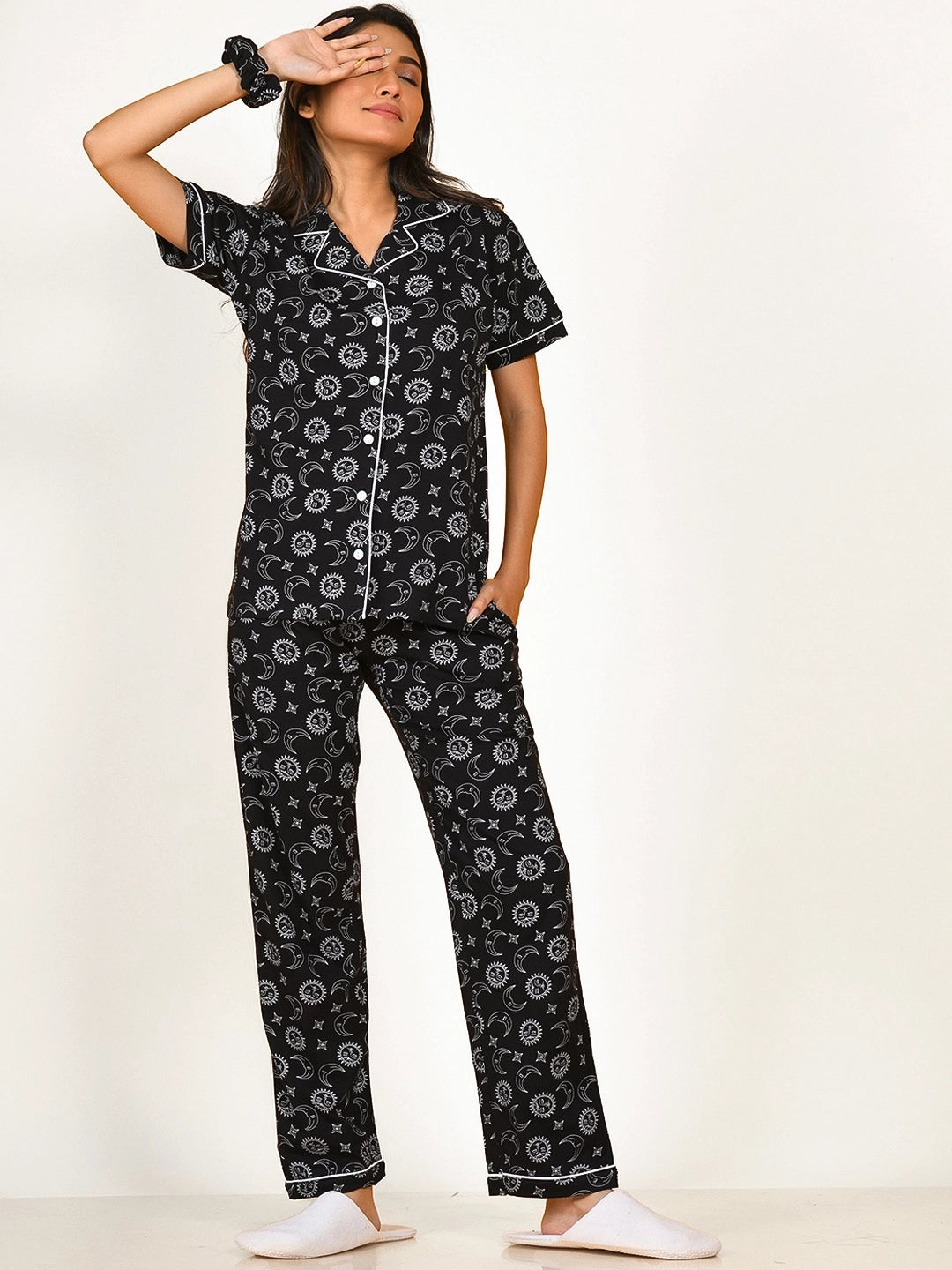 A girl wearing a black Star Moon Print Pyjama Set nightwear by NapStory, gently resting one hand on her eye and the other hand tucked away.