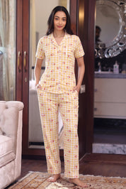 Woman wearing a yellow patterned pajama set in a room with a mirror and chair.