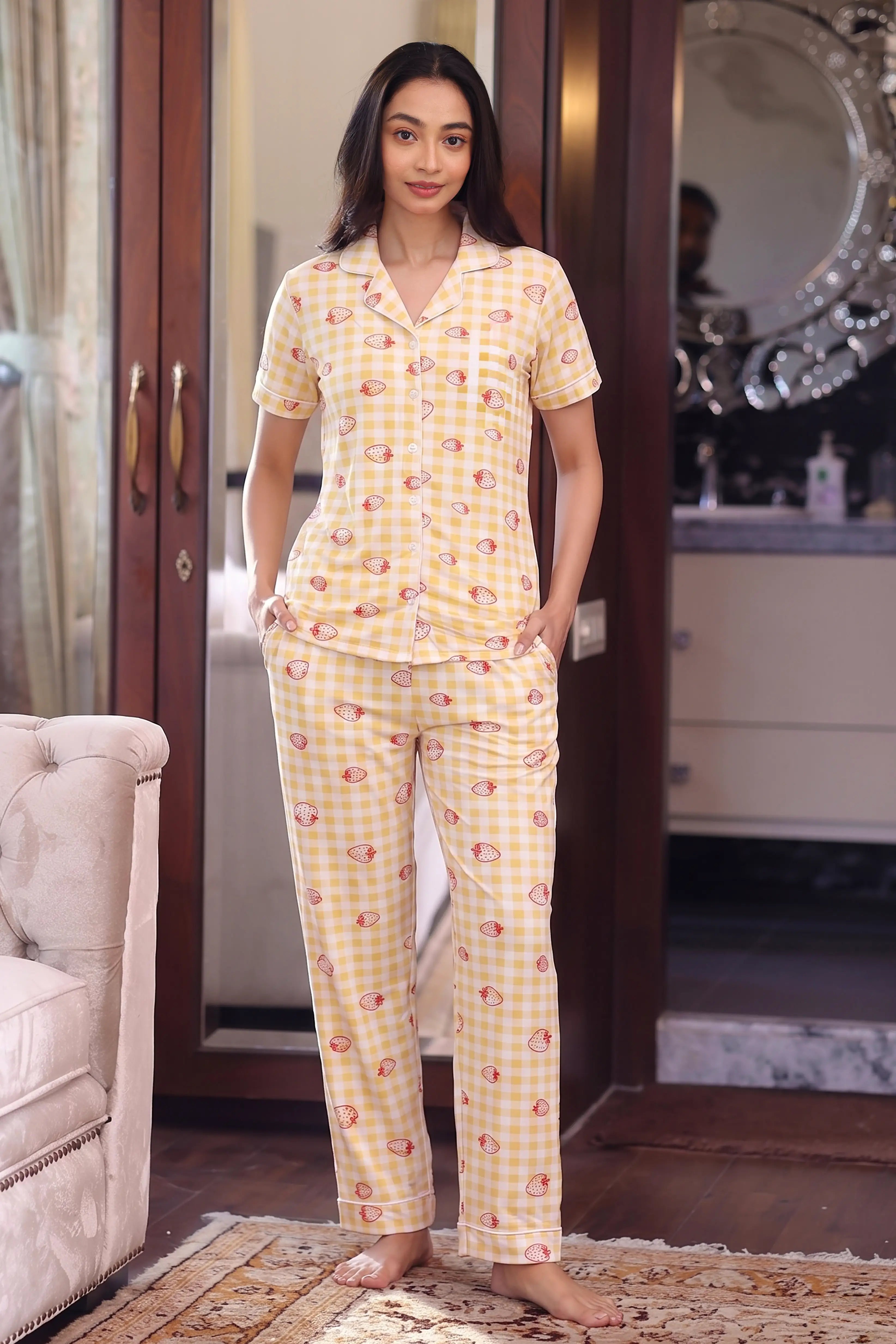 Woman wearing a yellow patterned pajama set in a room with a mirror and chair.
