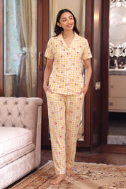 Woman wearing a yellow patterned pajama set standing in a room with a couch and decorative elements.