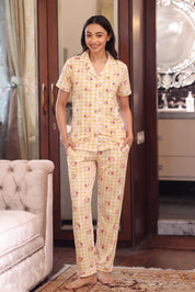 Woman wearing a yellow strawberry checkered pajama set in a room with a chair and decorative items.