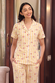 Woman wearing a yellow checkered pajama set with a strawberry pattern, standing in a room.