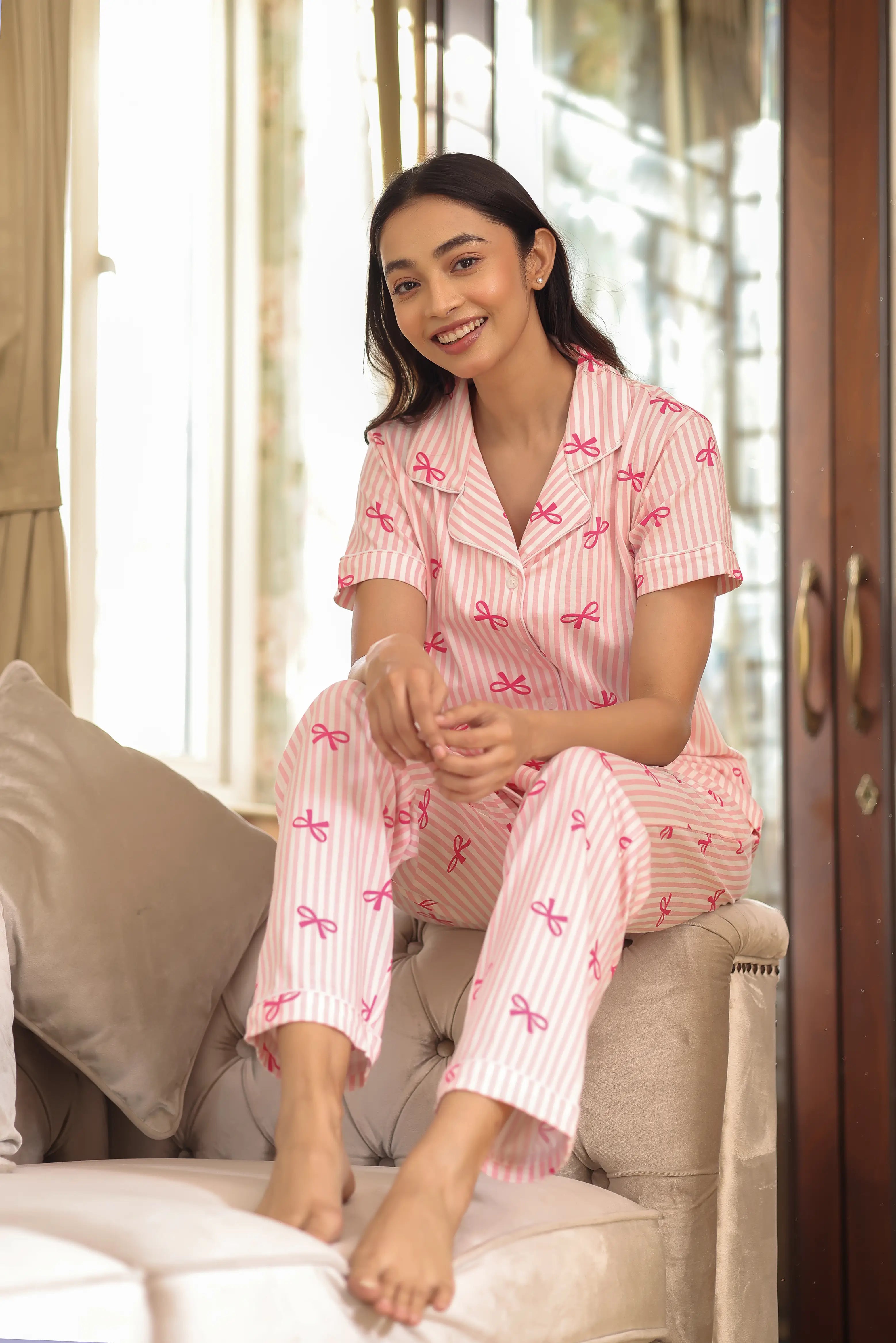 Woman wearing pink pajamas with bow patterns sitting on a couch.