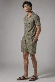Man wearing a green patterned shirt and shorts on a gray background